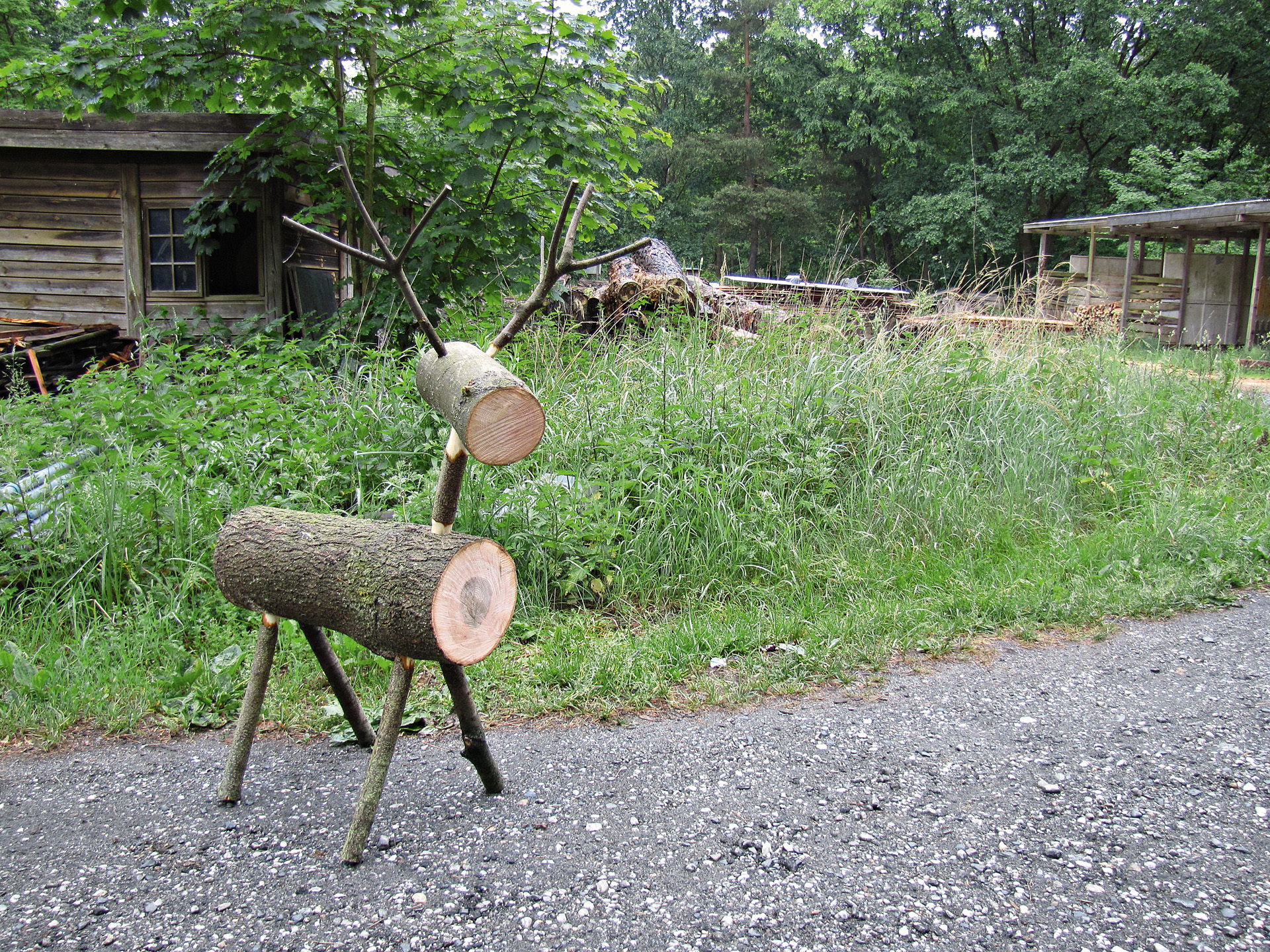 Drewniany renifer przed zielonym trawnikiem i drewnianą chatą